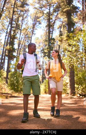 Young Active Couple Wearing Backpacks Hiking Along Trail Through Countryside Stock Photo