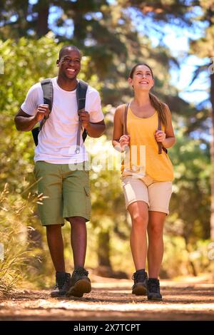 Young Active Couple Wearing Backpacks Hiking Along Trail Through Countryside Stock Photo