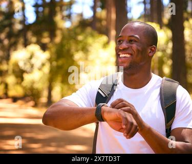 Young Active Man Checking Activity Monitor On Smart Watch Hiking Along Trail Through Countryside Stock Photo