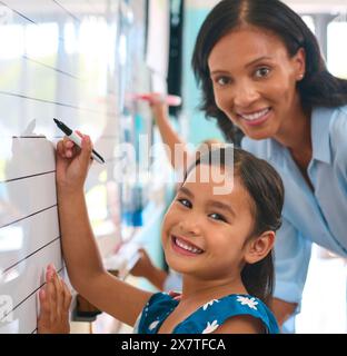 Portrait Of Primary Or Elementary School Student With Teacher Writing On Whiteboard In Lesson Stock Photo