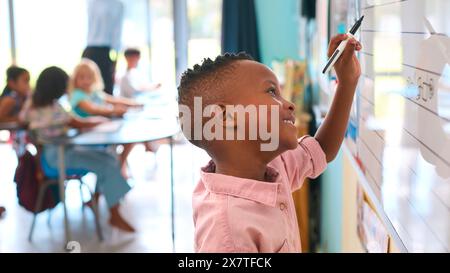 Male Primary Or Elementary School Student Writing On Whiteboard In Classroom Lesson Stock Photo