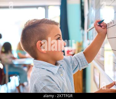 Male Primary Or Elementary School Student Writing On Whiteboard In Classroom Lesson Stock Photo