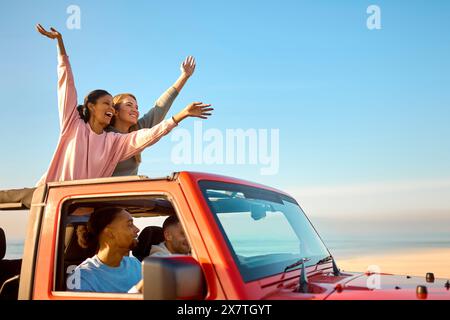 Couple With Friends On Vacation Driving Car On Road Trip Adventure To Beach Standing Up Through Roof Stock Photo