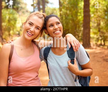 Portrait Of Two Female Friends Wearing Backpacks Hiking Along Trail Through Countryside Stock Photo