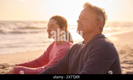 Peaceful Senior Couple Relaxing Sitting On Beach Shoreline With Closed Eyes At Sunrise Together Stock Photo