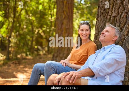 Retired Senior Couple Taking A Break Sitting At Base Of Tree On Hike Through Countryside Stock Photo