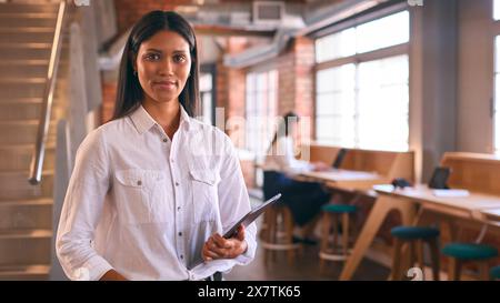 Portrait Of Young Smiling Businesswoman Holding Digital Tablet Working In Modern Open Plan Office Stock Photo