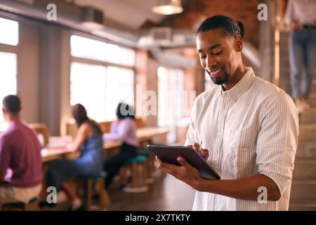 Businessman Using Digital Tablet And Stylus Pen Working In Busy Office With Colleagues In Background Stock Photo