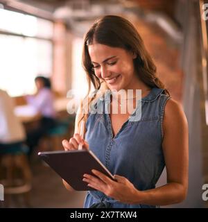 Businesswoman Using Digital Tablet And Stylus Pen Working In Office With Colleagues In Background Stock Photo