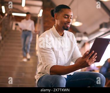 Businessman Using Digital Tablet Working In Busy Office With Colleagues In Background Stock Photo