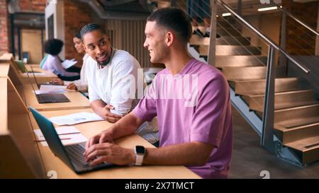 Two Businessmen With Laptop Meeting In Office Discussing Documents With Colleagues In Background Stock Photo