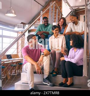 Smiling Multi-Cultural Business Team Sitting On Stairs In Modern Open Plan Office Stock Photo