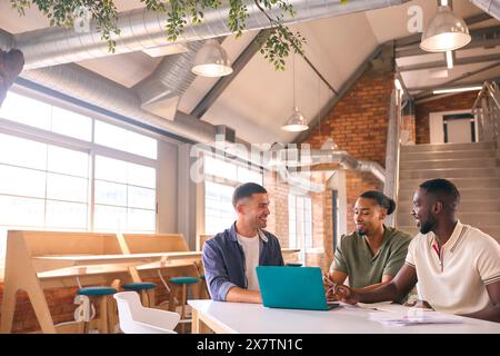 Three Businessmen Meeting In Modern Office Sitting Around Table Working On Laptop Together Stock Photo
