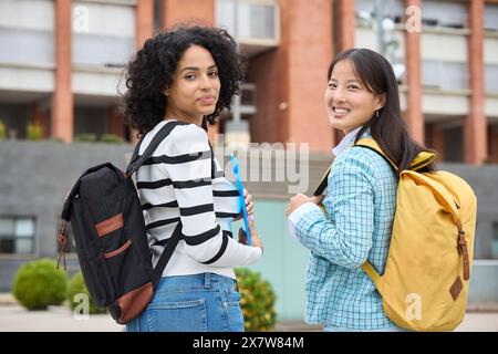 Two multiethnic students are smiling and holding backpacks Stock Photo