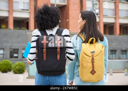 Two young students are walking down the street, each carrying a backpack Stock Photo
