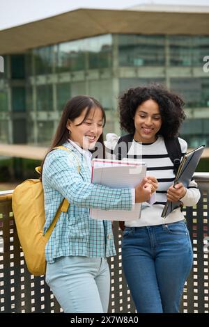 Two multiethnic students sharing notes outside the University Stock Photo