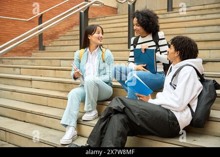 Three young people are sitting on a set of stairs, each holding a book Stock Photo