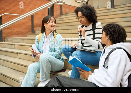Three young students are sitting on steps, one of them holding a book Stock Photo