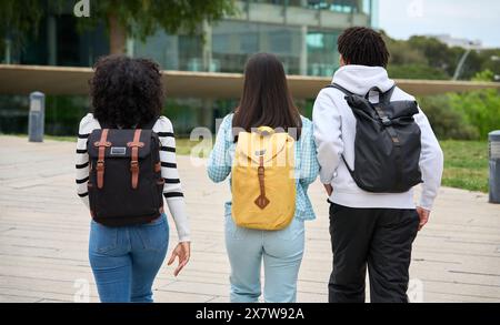 Three young students walking down a sidewalk to the University, each carrying a backpack Stock Photo