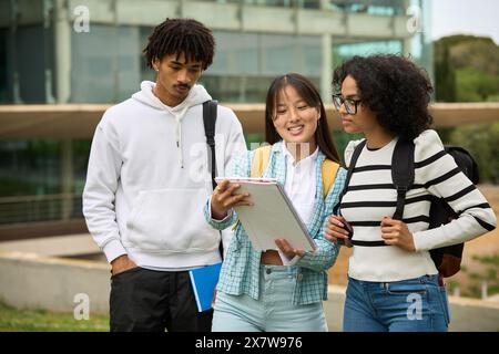 Three young students are standing outside a building sharing notes Stock Photo