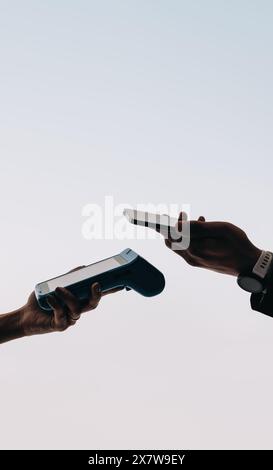 Hands holding a smartphone and a card machine close to each other, making a contactless mobile payment. Two people transacting using NFC technology. Stock Photo