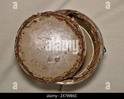 Rusted old metal paint tin with open lid on drop cloth brown expired storage. Stock Photo