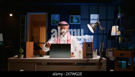 Arab employee arriving in stylish apartment personal office, starting important job tasks. Focused muslim teleworker typing on laptop keyboard, beginning work shift at home Stock Photo