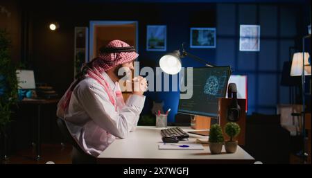 Licensed arabic engineer updating neural networks, writing intricate binary code scripts on computer. Middle Eastern man uses digital device programming to upgrade AI datasets at home Stock Photo