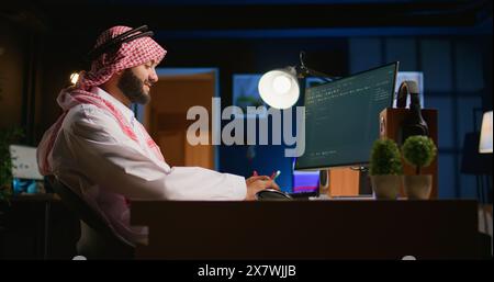 Smiling muslim engineer writing script code on computer screen using Java programming languages. Self employed Middle Eastern developer at home working on fixing database errors Stock Photo