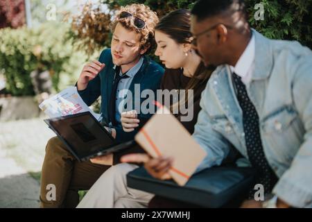 Three diverse professionals collaborating outdoors with a laptop and documents Stock Photo