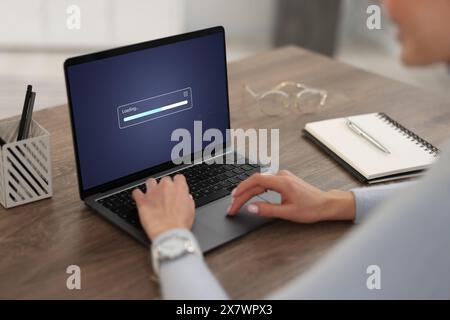 Loading screen displaying progress. Woman working on laptop at table indoors, closeup Stock Photo