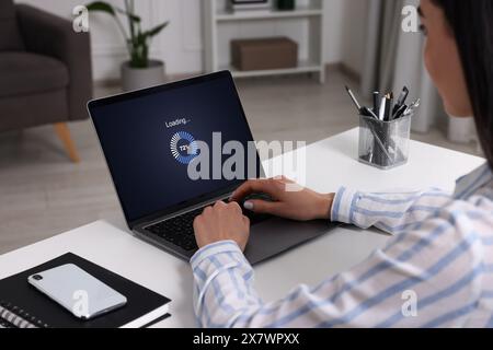 Loading screen displaying progress. Woman working on laptop at table indoors, closeup Stock Photo