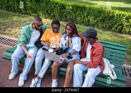 Four african american students girls and guys looking at screen laptop while coffee break outdoor. Stock Photo