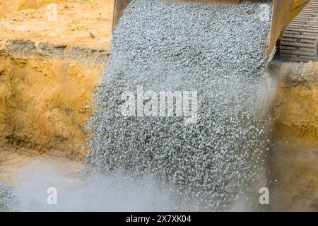 During excavations, an excavator fills irregularities with granite rubble base to be submerged in concrete foundation Stock Photo