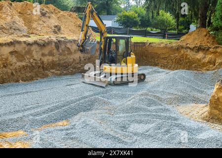 An excavator fills irregularities in excavations with granite rubble base to serve as foundation for concrete Stock Photo