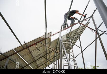 Man engineer standing on metal rail and using electric drill while installing support structure for photovoltaic solar panels. Isolated on white background. Stock Photo