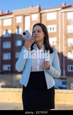 Confident young businesswoman using voice recognition function on a smartphone. Modern female entrepreneur outdoors, sending a vocal message via onlin Stock Photo
