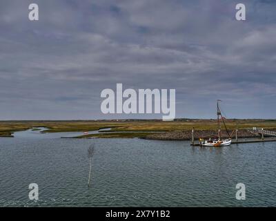Sailboat at a jetty surrounded by a watery landscape under a cloudy sky, small jetty with a mono-sea sailboat in the north sea against a cloudy sky, s Stock Photo