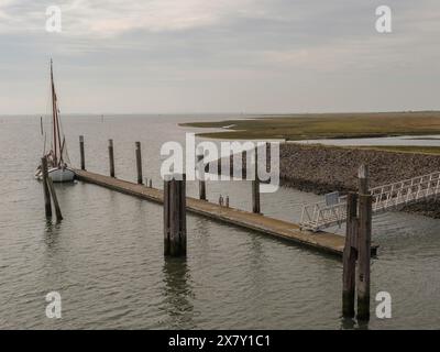 A sailboat is moored at a jetty under an overcast sky by the sea, small jetty with a one-seater sailboat in the north sea against a cloudy sky, spieke Stock Photo
