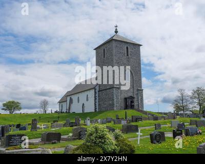 Stone church on a hill surrounded by a cemetery with numerous gravestones under a cloudy sky, old stone church and many gravestones by the water with Stock Photo