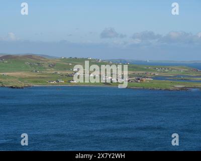 Small settlement with white houses stretches along the grassy coastline in front of the blue sea, green meadows on a deep blue sea and a rocky coastli Stock Photo