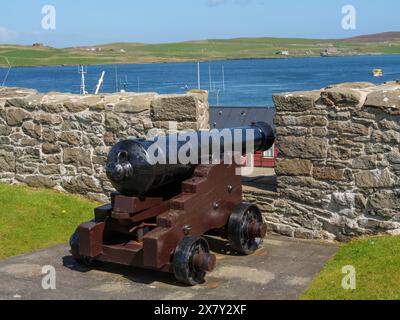 Old cannon in front of a stone wall with a view of the sea and green hills in the background, old cannon on a stone wall by the sea against a blue sky Stock Photo