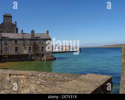 Historic stone wall and houses overlooking the sea and harbour with boats, old stone house by the blue sea against a blue sky, Lerwick, Scotland, Unit Stock Photo