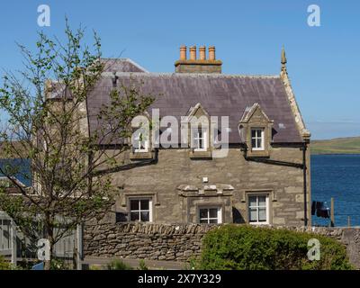 A stone house with fireplaces next to a tree, coastal landscape, blue sky and sea, old stone house by the blue sea against a blue sky, Lerwick, Scotla Stock Photo