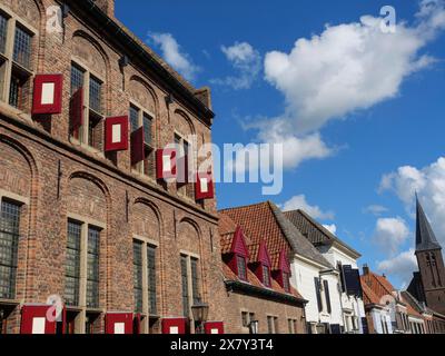 Historic building with red shutters and accompanying houses under a blue sky with clouds, historic house with red and white shutters and flower decora Stock Photo
