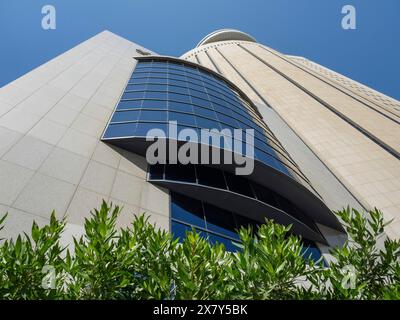 View upwards to a modern skyscraper with glass facade and plants in the foreground under a blue sky, modern skyscrapers with glass facades and many wi Stock Photo