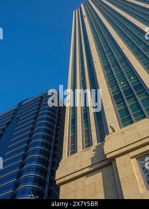 View upwards to a modern skyscraper with glass facade and concrete structures under a clear sky, modern skyscrapers with glass facades and many window Stock Photo