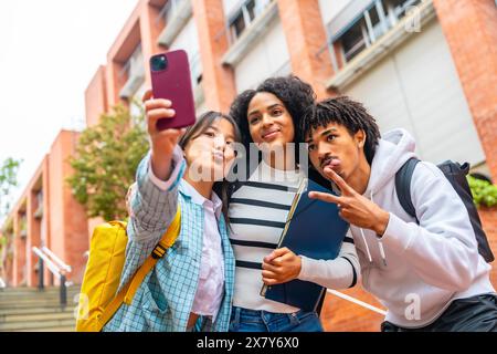 Low angle view portrait of three happy multiracial university students taking a selfie outside the campus Stock Photo