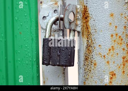 Small closed padlock hanging on the hinges Stock Photo