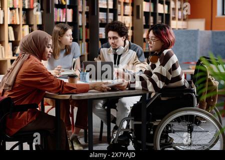 Group of diverse male and female students spending time together studying in library Stock Photo